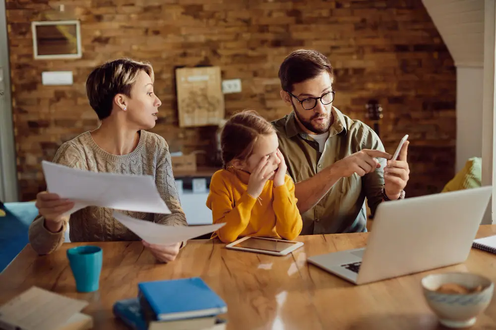 Family budgeting together at home using bills, laptop, and smartphone