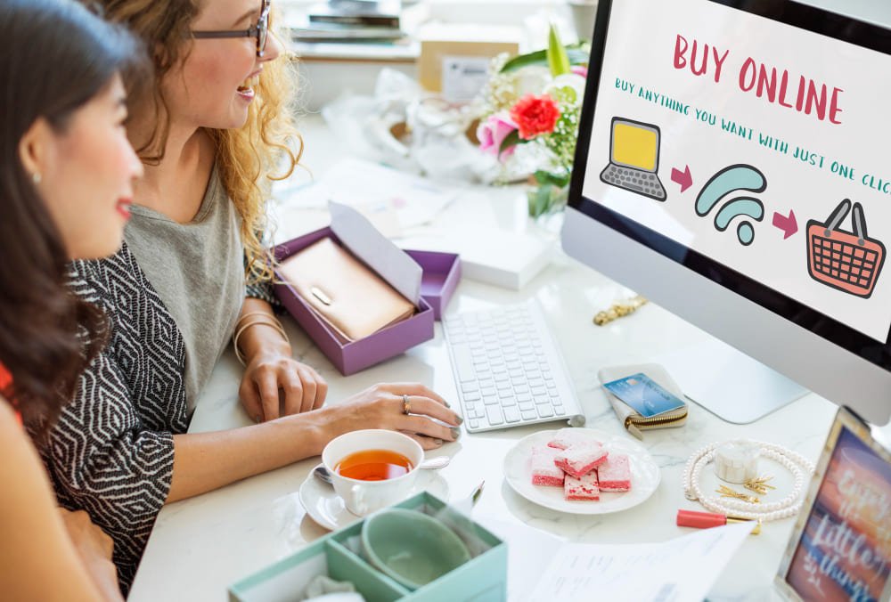 Two women shopping for digital products online using a desktop computer — illustrating how to buy and sell online in 2025.