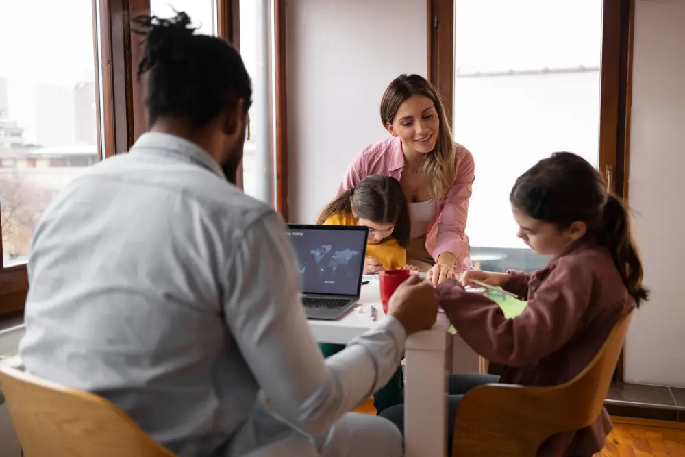 Parents and children working together at the kitchen table, discussing finances with a laptop open—representing a collaborative family budgeting session.